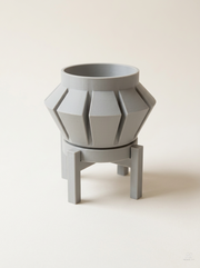 Vaso Erno sfaccettato con costole a punta di freccia, con sottovaso e supporto a quattro gambe, stampato in 3D in PLA grigio chiaro.