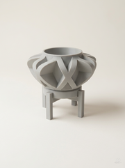 Vaso Sono avvolto da fasce incrociate a X come una gabbia, con sottovaso e supporto a quattro gambe, stampato in 3D in PLA grigio chiaro.
